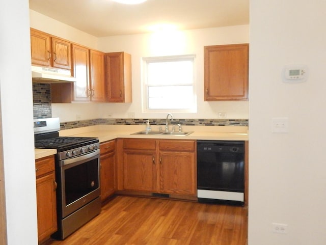 kitchen with black dishwasher, stainless steel gas range, light countertops, under cabinet range hood, and a sink