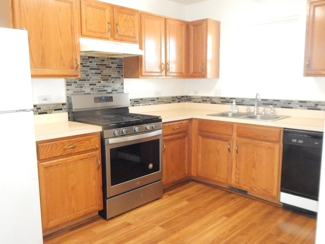 kitchen with black dishwasher, freestanding refrigerator, a sink, gas range, and under cabinet range hood