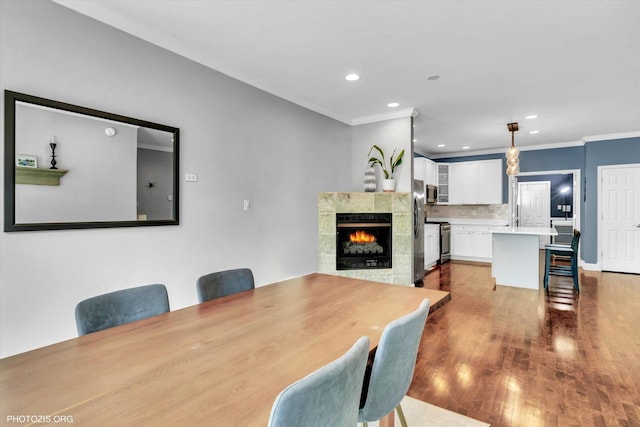 dining room featuring wood finished floors, ornamental molding, a tile fireplace, and recessed lighting