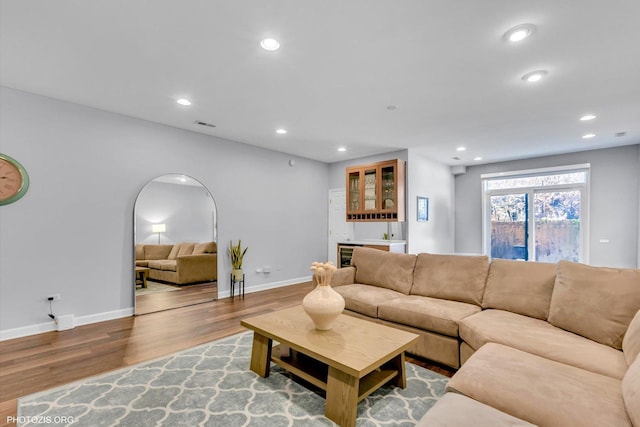 living room with arched walkways, recessed lighting, wood finished floors, bar, and baseboards