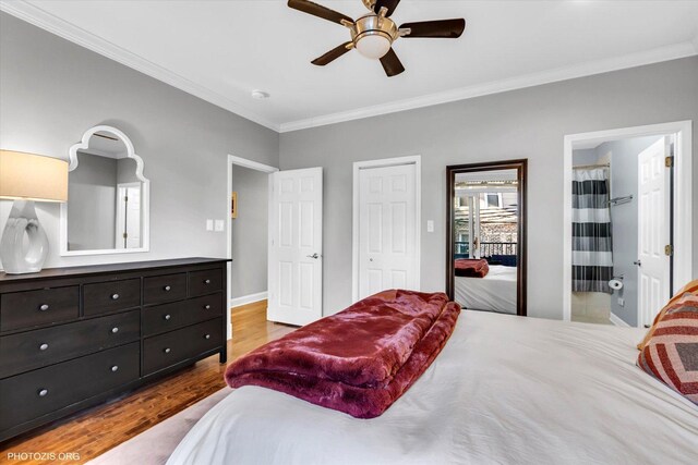 bedroom with wood finished floors, a ceiling fan, baseboards, ensuite bath, and crown molding