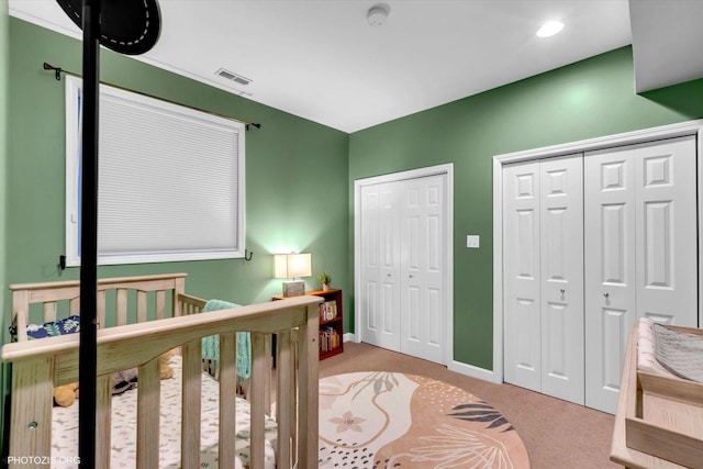 bedroom with a crib, baseboards, visible vents, carpet flooring, and multiple closets