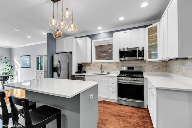 kitchen with a sink, white cabinets, ornamental molding, appliances with stainless steel finishes, and a kitchen bar