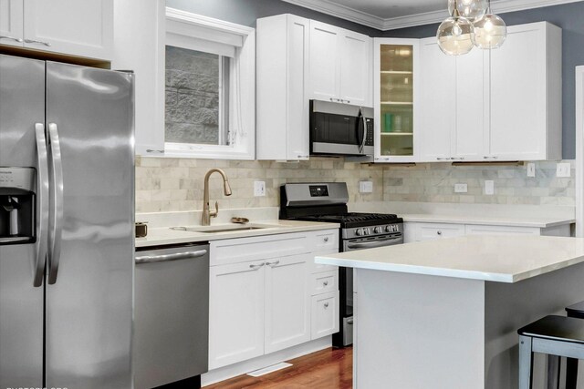 kitchen featuring tasteful backsplash, white cabinets, ornamental molding, stainless steel appliances, and a sink