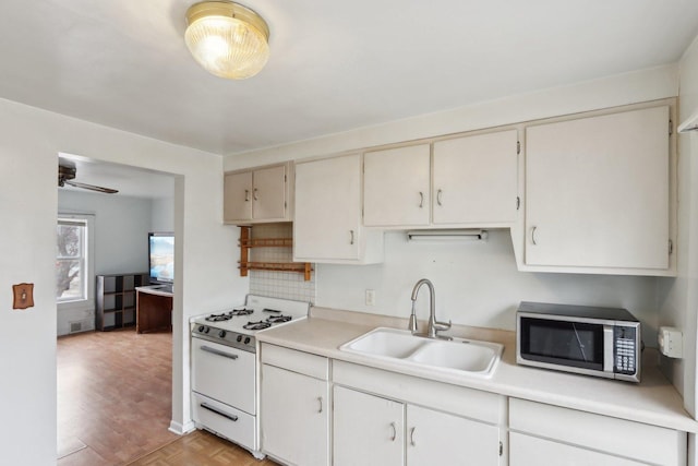 kitchen with white gas range oven, decorative backsplash, stainless steel microwave, light countertops, and a sink