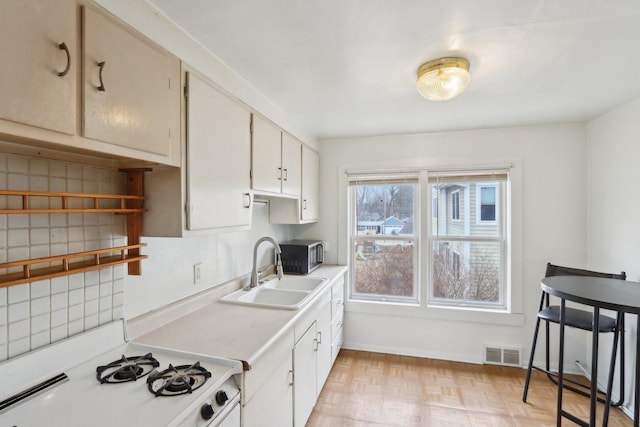 kitchen featuring white range with gas cooktop, visible vents, decorative backsplash, light countertops, and a sink