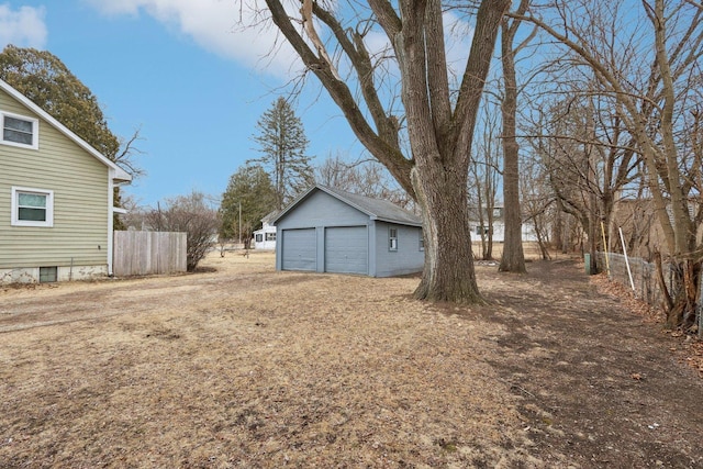 view of yard featuring a detached garage, fence, and an outbuilding