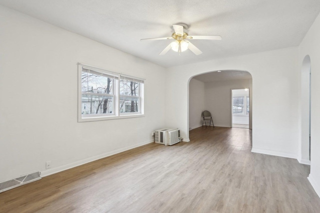 unfurnished room with arched walkways, a ceiling fan, baseboards, visible vents, and light wood-style floors