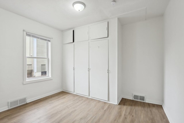 unfurnished bedroom with light wood-type flooring, baseboards, visible vents, and a closet