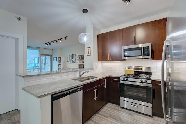 kitchen with a peninsula, a sink, appliances with stainless steel finishes, light stone countertops, and tasteful backsplash