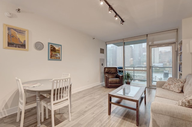 living area featuring a view of city, floor to ceiling windows, light wood-style flooring, track lighting, and baseboards