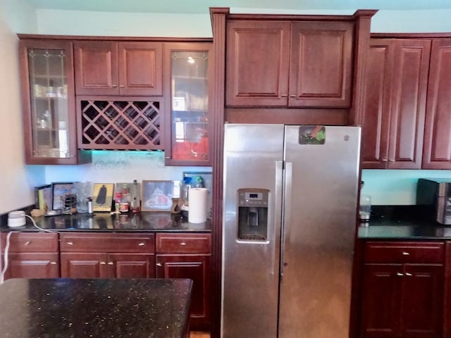 kitchen with dark stone counters, glass insert cabinets, and stainless steel fridge with ice dispenser