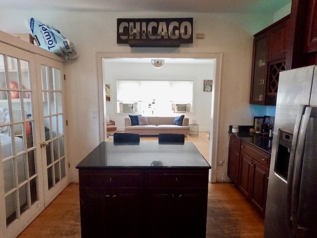 kitchen featuring wood finished floors, a kitchen island, french doors, dark countertops, and stainless steel fridge