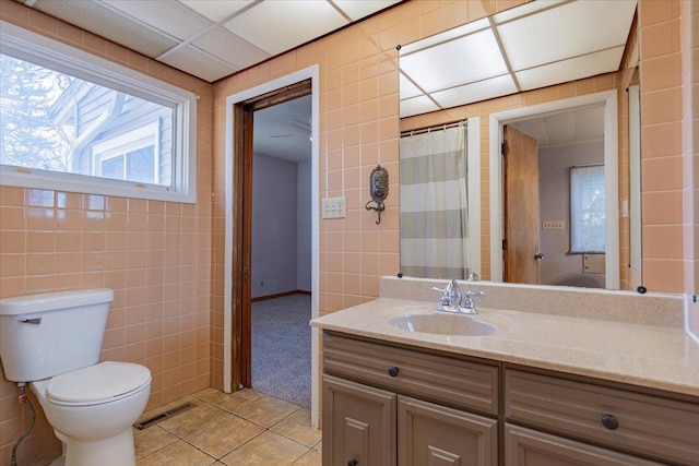 bathroom with tile patterned flooring, toilet, visible vents, vanity, and tile walls