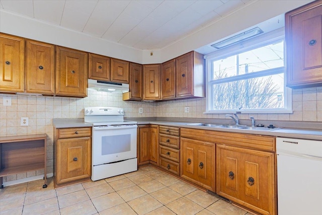 kitchen featuring under cabinet range hood, white appliances, a sink, decorative backsplash, and brown cabinets