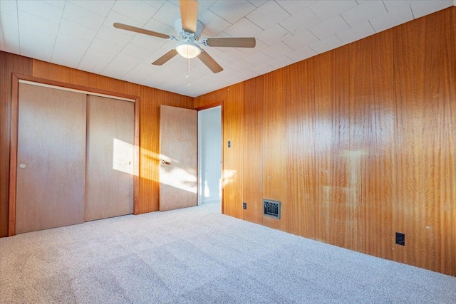 unfurnished bedroom featuring wood walls, a closet, visible vents, and carpet flooring