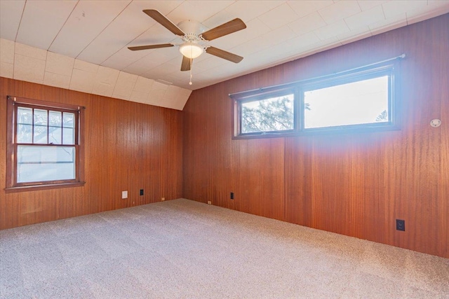 spare room with ceiling fan, wooden walls, vaulted ceiling, and carpet flooring