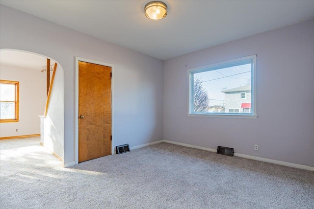 unfurnished room with baseboards, visible vents, arched walkways, and carpet flooring