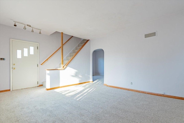 unfurnished living room with arched walkways, visible vents, stairway, and carpet