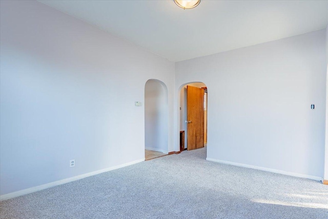 empty room with baseboards, arched walkways, vaulted ceiling, and carpet flooring