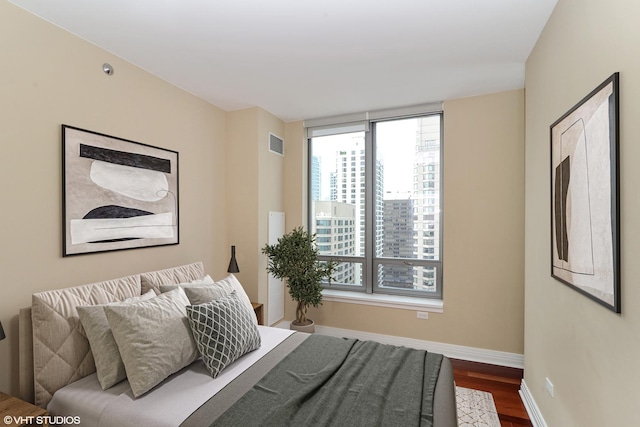 bedroom featuring dark wood-type flooring, a view of city, visible vents, and baseboards