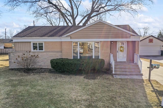 view of front of home with an outdoor structure, brick siding, a front yard, and roof with shingles