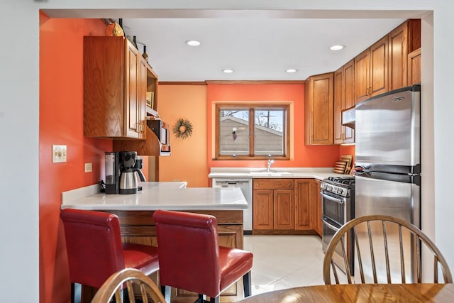 kitchen with brown cabinets, a sink, appliances with stainless steel finishes, a peninsula, and light countertops