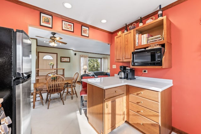 kitchen featuring a peninsula, freestanding refrigerator, light countertops, black microwave, and crown molding