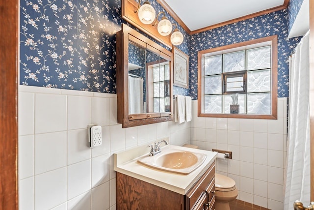 bathroom with wallpapered walls, toilet, vanity, and wainscoting