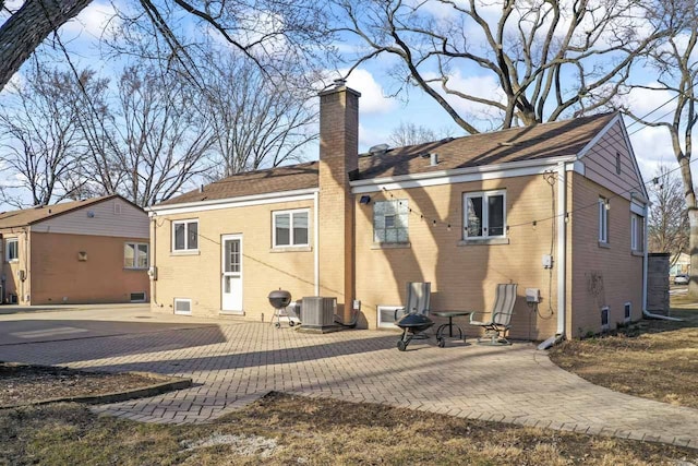 rear view of house with brick siding, central AC unit, a chimney, and a patio