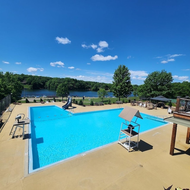 pool with a water slide, a water view, fence, and a patio