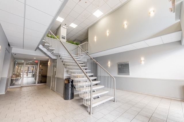 staircase with a high ceiling, a paneled ceiling, and baseboards