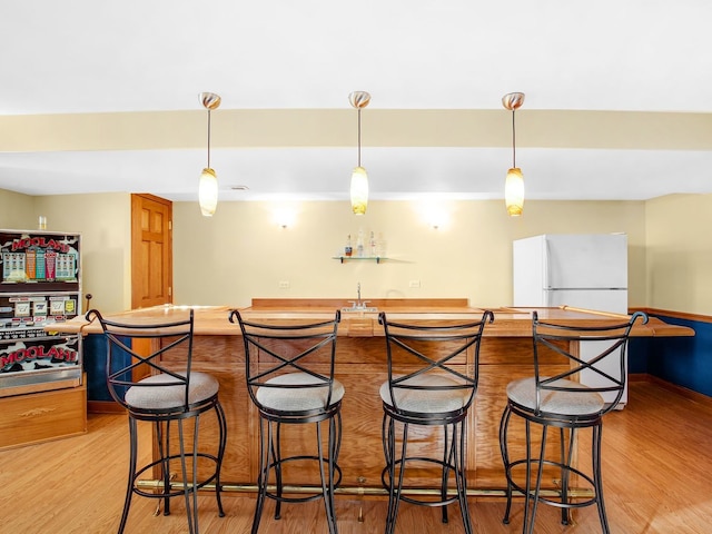 kitchen featuring light wood-type flooring, hanging light fixtures, a sink, and freestanding refrigerator