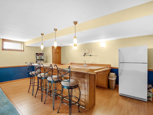 kitchen featuring butcher block countertops, freestanding refrigerator, light wood-style floors, a kitchen bar, and pendant lighting