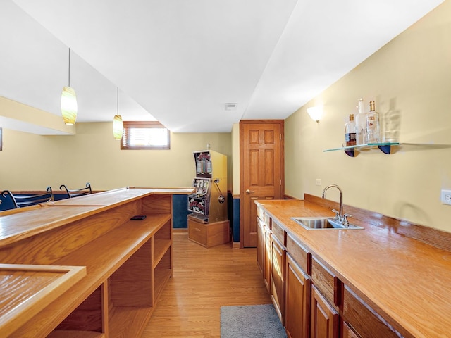 kitchen featuring brown cabinets, decorative light fixtures, light countertops, light wood-type flooring, and a sink