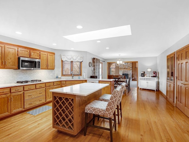 kitchen with a skylight, a kitchen island, appliances with stainless steel finishes, light countertops, and a sink