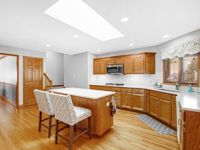 kitchen featuring a skylight, a center island, appliances with stainless steel finishes, light wood-style floors, and a sink