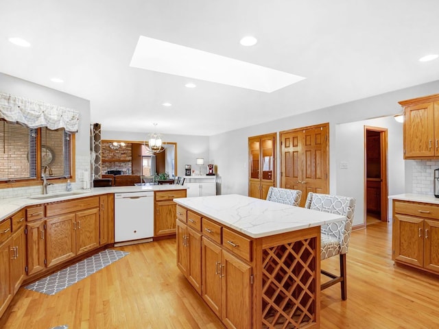 kitchen with a skylight, tasteful backsplash, light wood-style flooring, a sink, and dishwasher