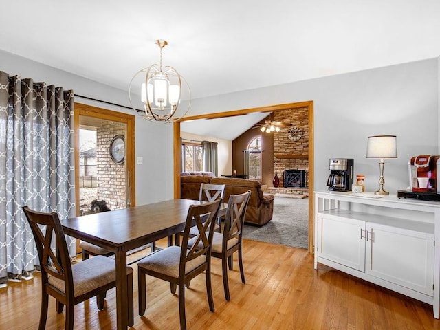 dining space with lofted ceiling, light wood-type flooring, ceiling fan with notable chandelier, and a stone fireplace