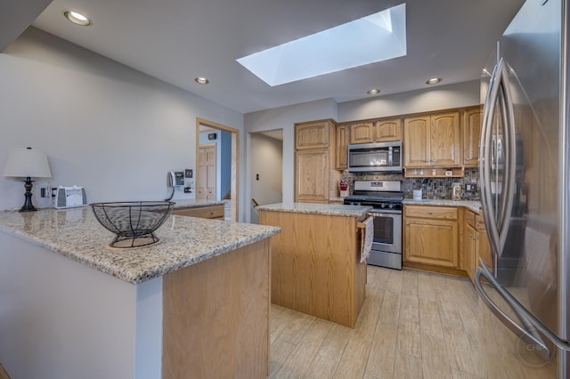 kitchen with a peninsula, a skylight, a kitchen island, appliances with stainless steel finishes, and backsplash