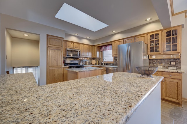 kitchen featuring a skylight, backsplash, appliances with stainless steel finishes, glass insert cabinets, and a kitchen island