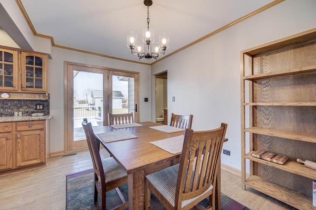 dining room with baseboards, ornamental molding, light wood-style flooring, and a notable chandelier