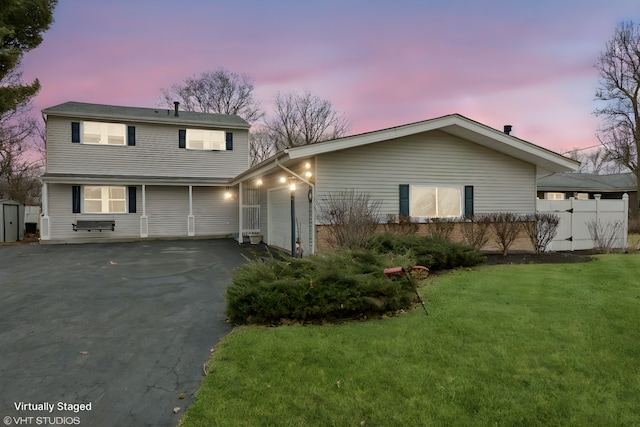 view of front of house with fence, an attached garage, an outdoor structure, aphalt driveway, and a lawn