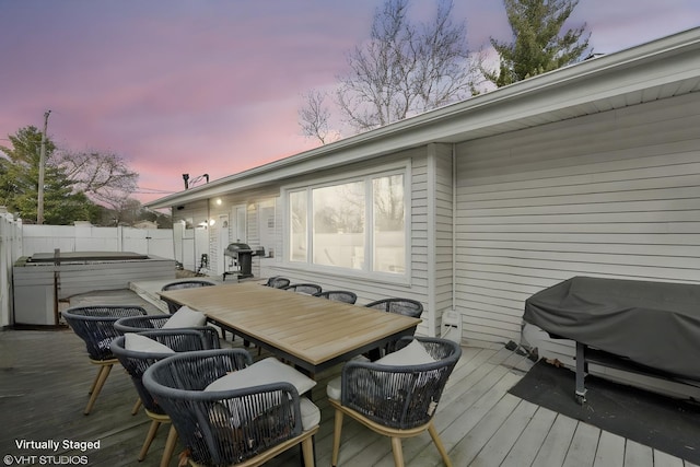 deck at dusk with outdoor dining space, a jacuzzi, a fenced backyard, and area for grilling