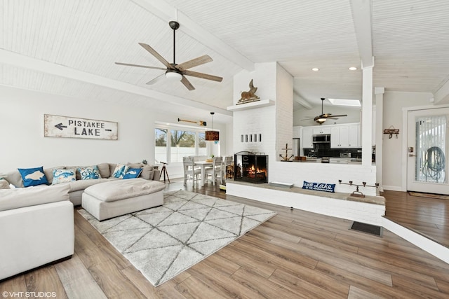 living room with baseboards, ceiling fan, beamed ceiling, a fireplace, and wood finished floors