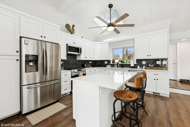 kitchen featuring stainless steel appliances, a kitchen breakfast bar, white cabinets, and vaulted ceiling with beams