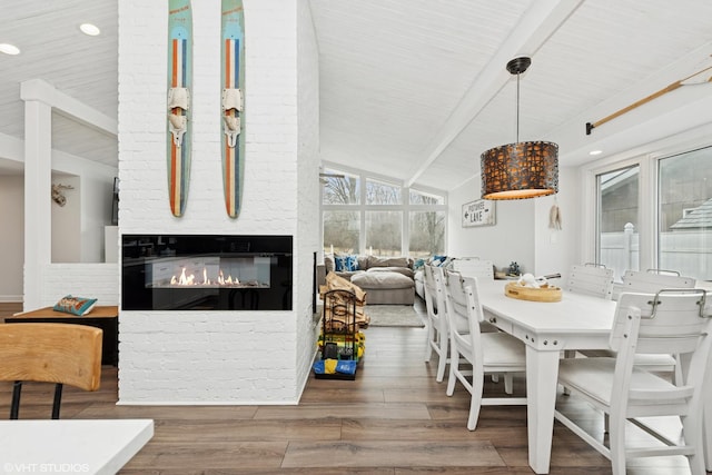 dining area featuring a glass covered fireplace, lofted ceiling with beams, and wood finished floors