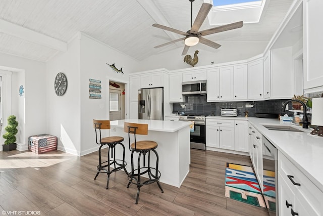 kitchen featuring a breakfast bar area, wood finished floors, a sink, appliances with stainless steel finishes, and tasteful backsplash