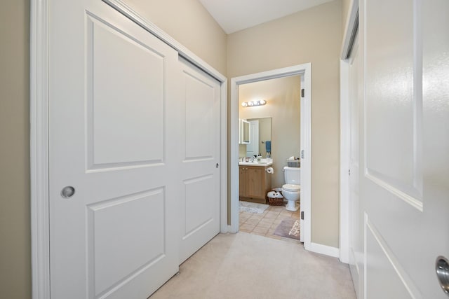 hall featuring baseboards, a sink, and light colored carpet