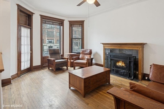 living room with a fireplace, a ceiling fan, baseboards, ornamental molding, and hardwood / wood-style floors